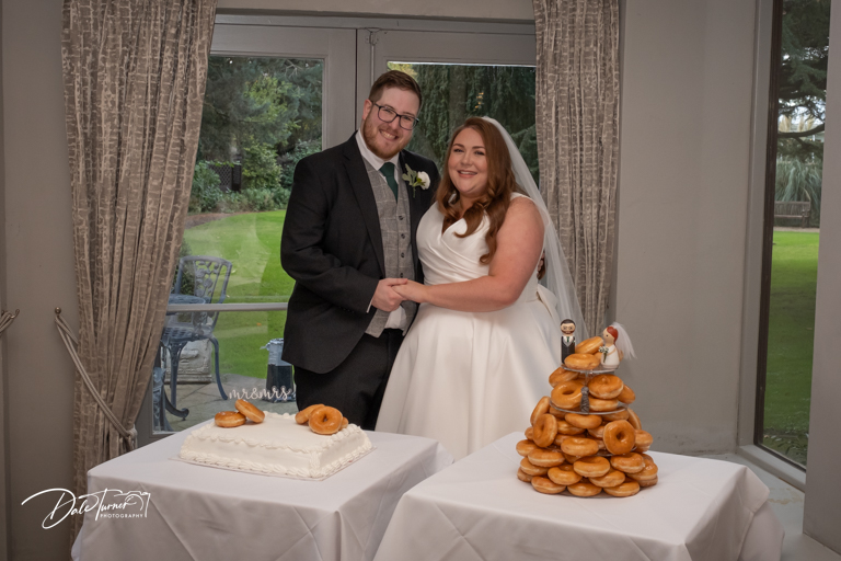 Couple with wedding cake and doughnut tower at reception.