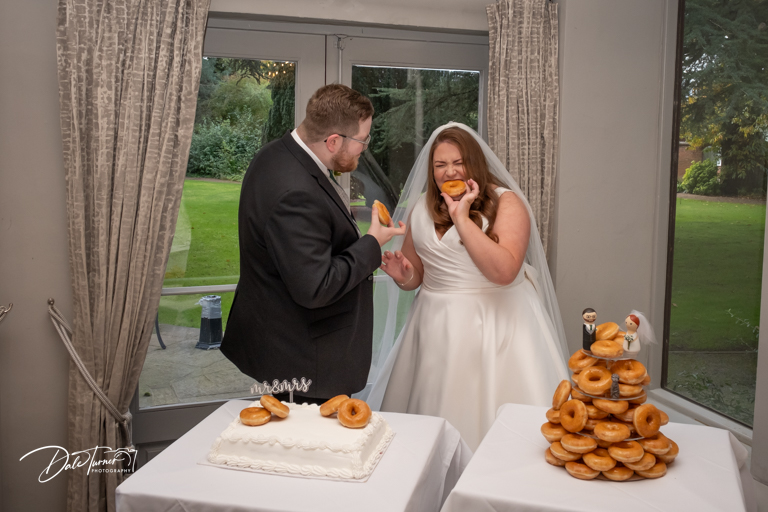 Bride and groom laughing with doughnuts at wedding reception.