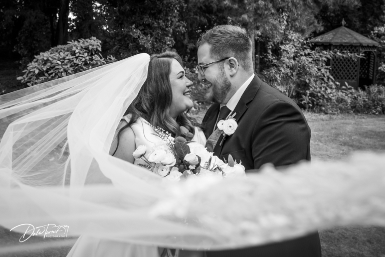Bride and groom smiling outdoors, black and white photo.