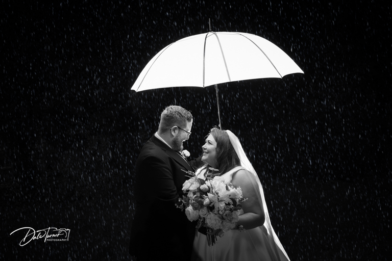 Bride and groom with an umbrella in black and white rain wedding photo.