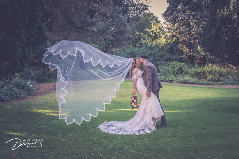 Couple kissing in garden of The Parsonage, bride's veil billowing.