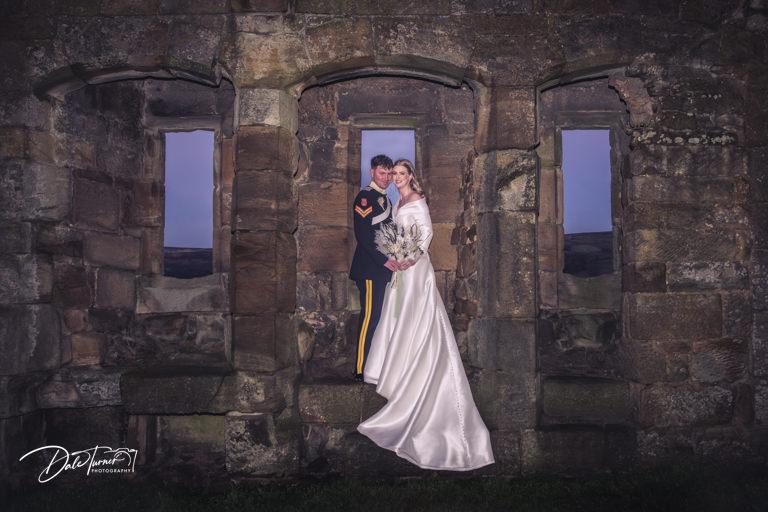 Couple in wedding attire posing in historic ruin at dusk.