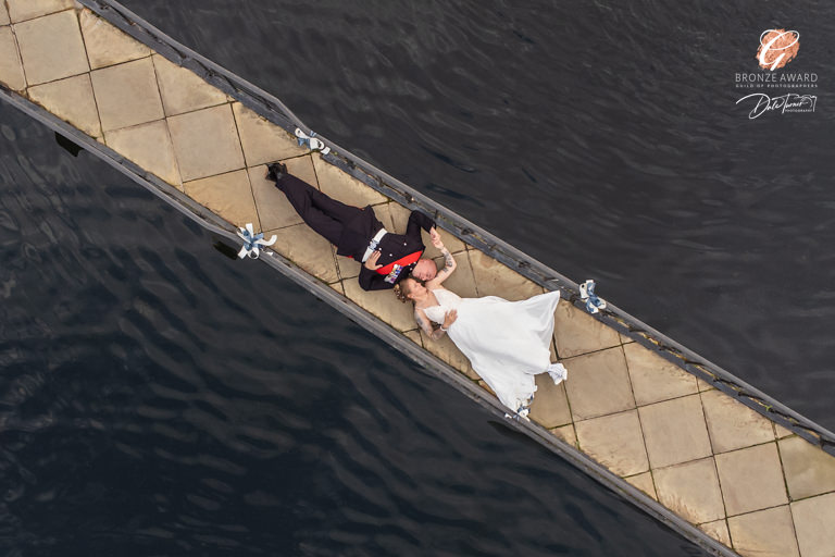 Bridal couple lying on dock by water, aerial view.