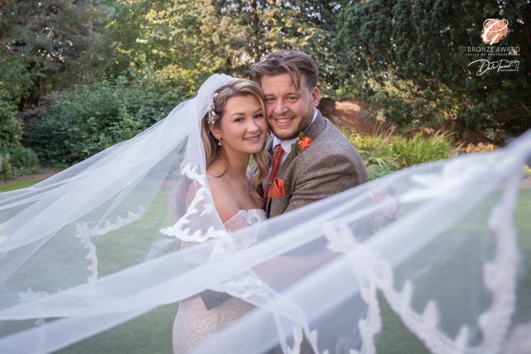 Bride and groom smiling under flowing wedding veil.