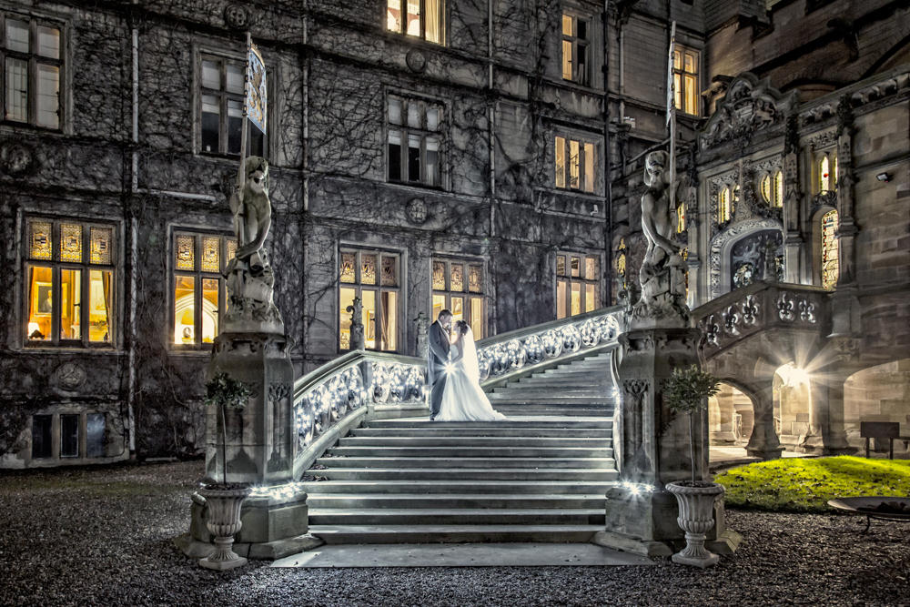 Bride & groom on illuminated stairs of historic mansion at night