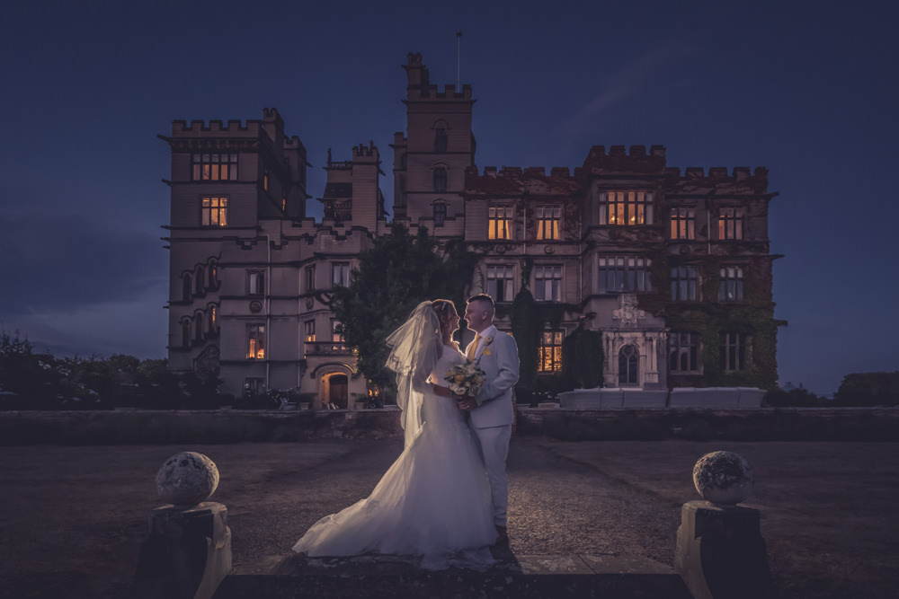 Bride and groom embracing outside a grand estate at dusk
