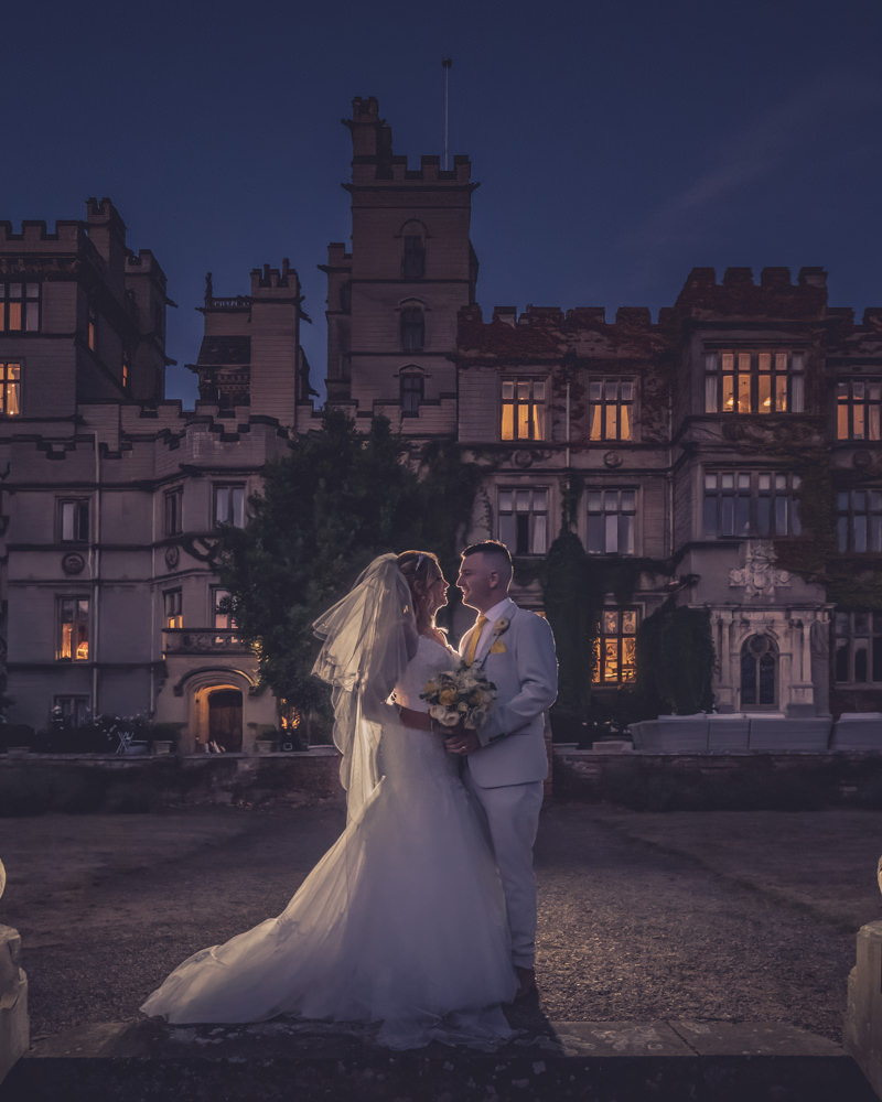 Newlyweds outside historic castle at dusk.