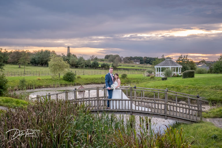 Couple on bridge in scenic park at sunset.