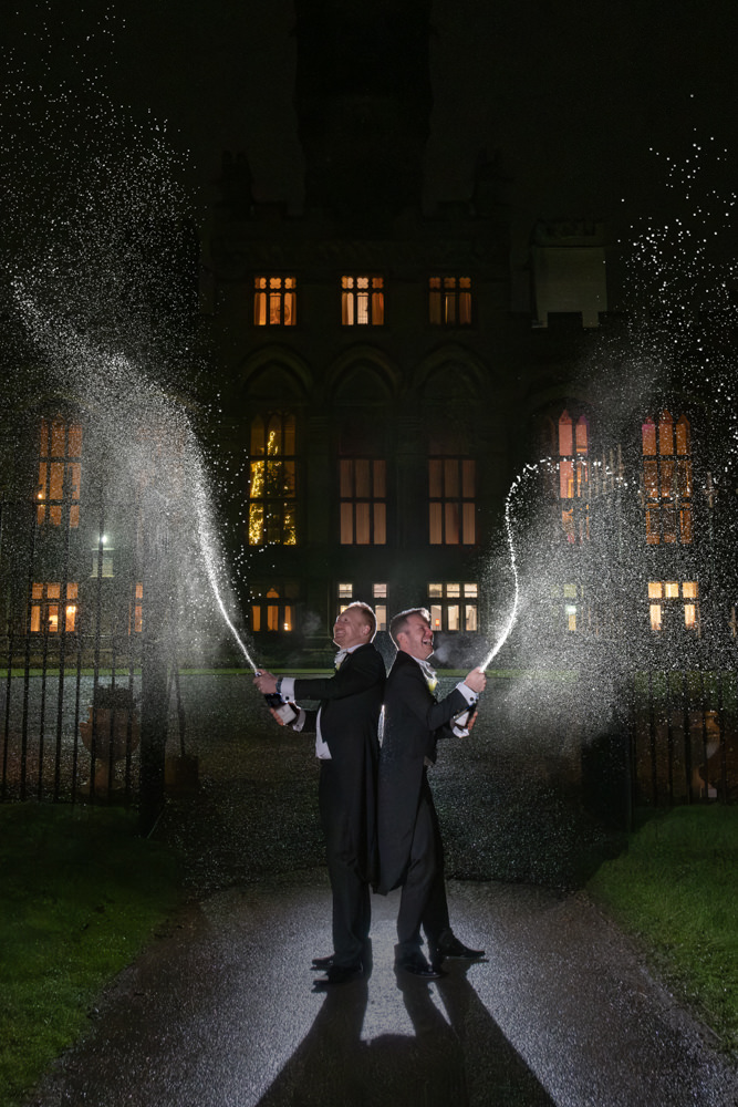 Men spraying champagne at night in front of Carlton Towers